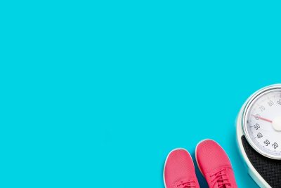 Różowe buty sportowe obok wagi łazienkowej na niebieskim tle