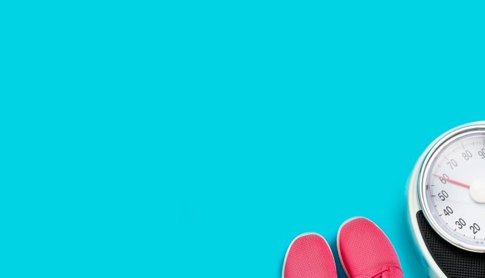 Różowe buty sportowe obok wagi łazienkowej na niebieskim tle