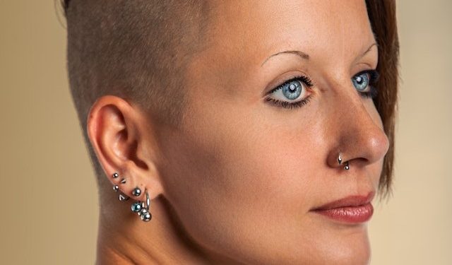Kobieta z wygolonymi włosami z kolczykami w uchu i na nosie