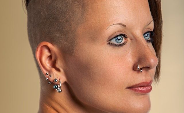 Kobieta z wygolonymi włosami z kolczykami w uchu i na nosie